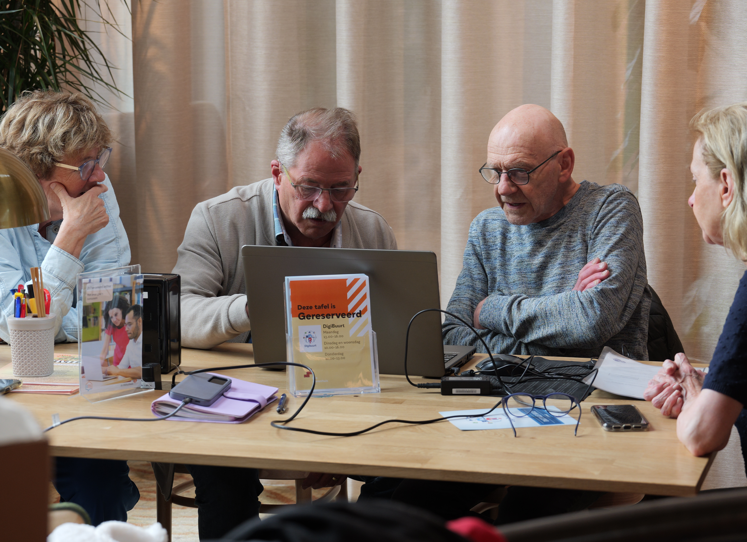 het warenhuis oss Digibuurt, mensen aan tafel die anderen aan het helpen zijn met een laptop.